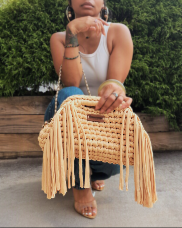 Tan crochet fringe bag with leather Harper & Hammer tag held by strap outdoors