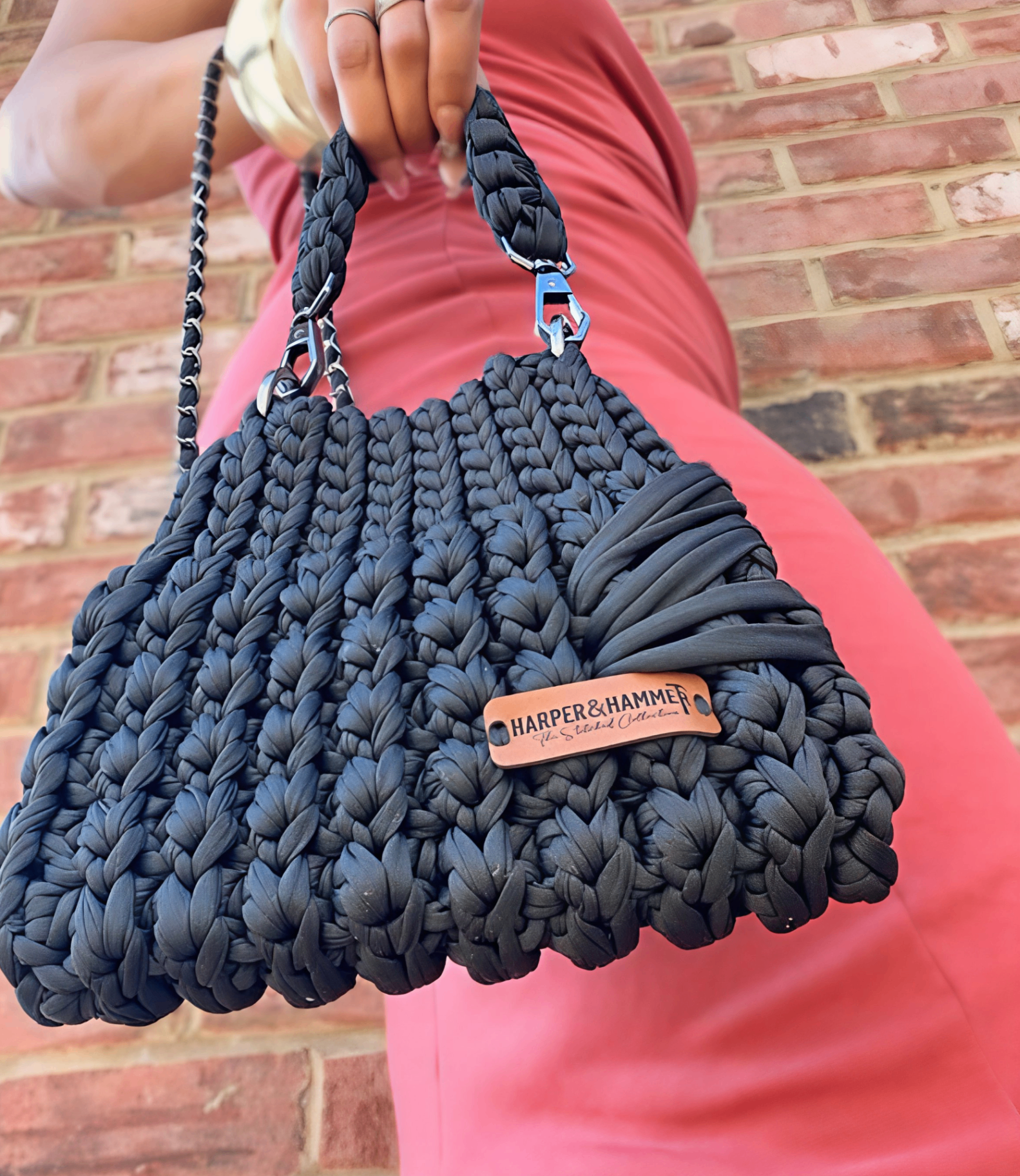 Black Harper & Hammer crochet bag with leather brand tag against a brick wall