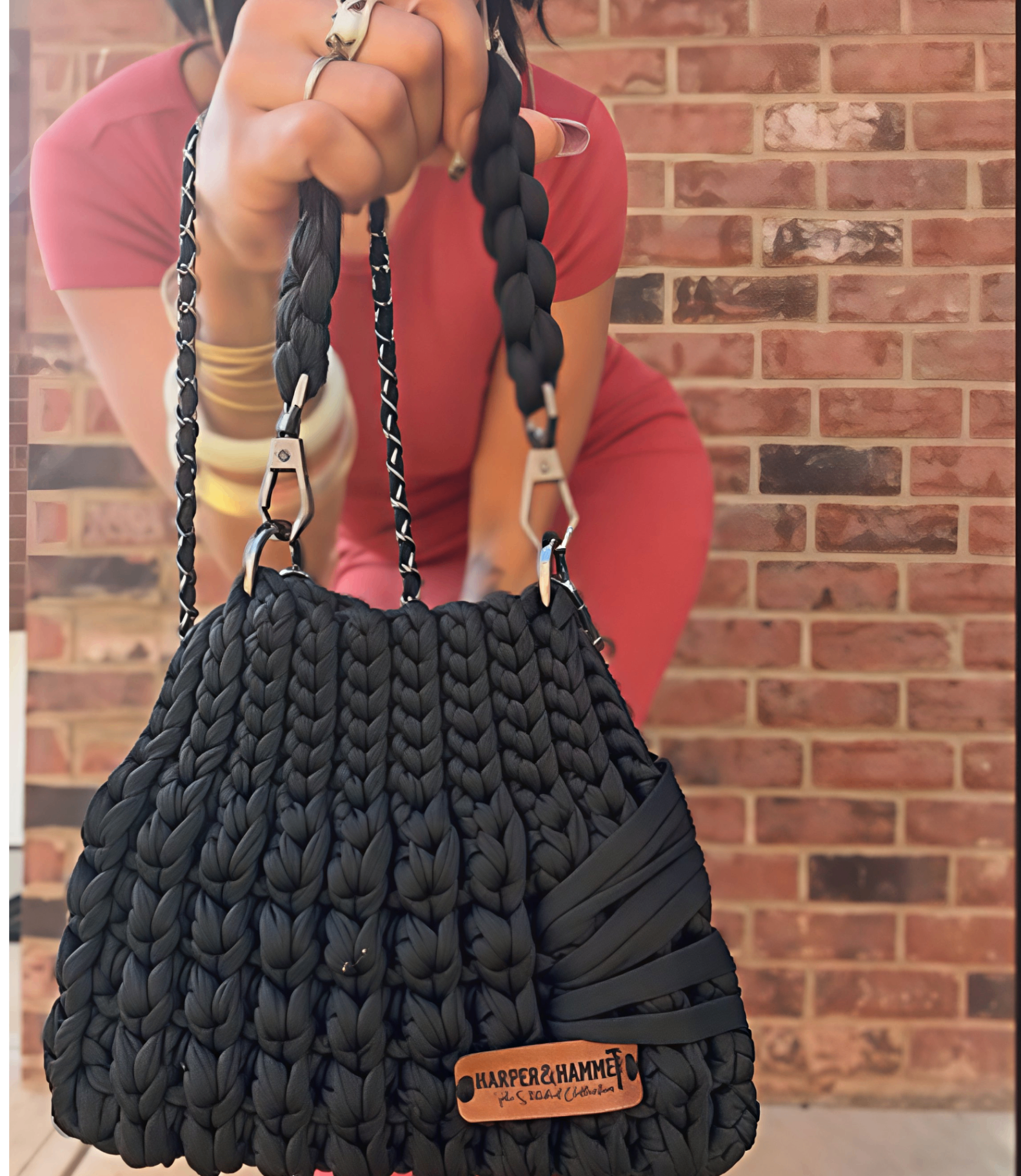Black crochet bag with braided straps held up against a brick wall