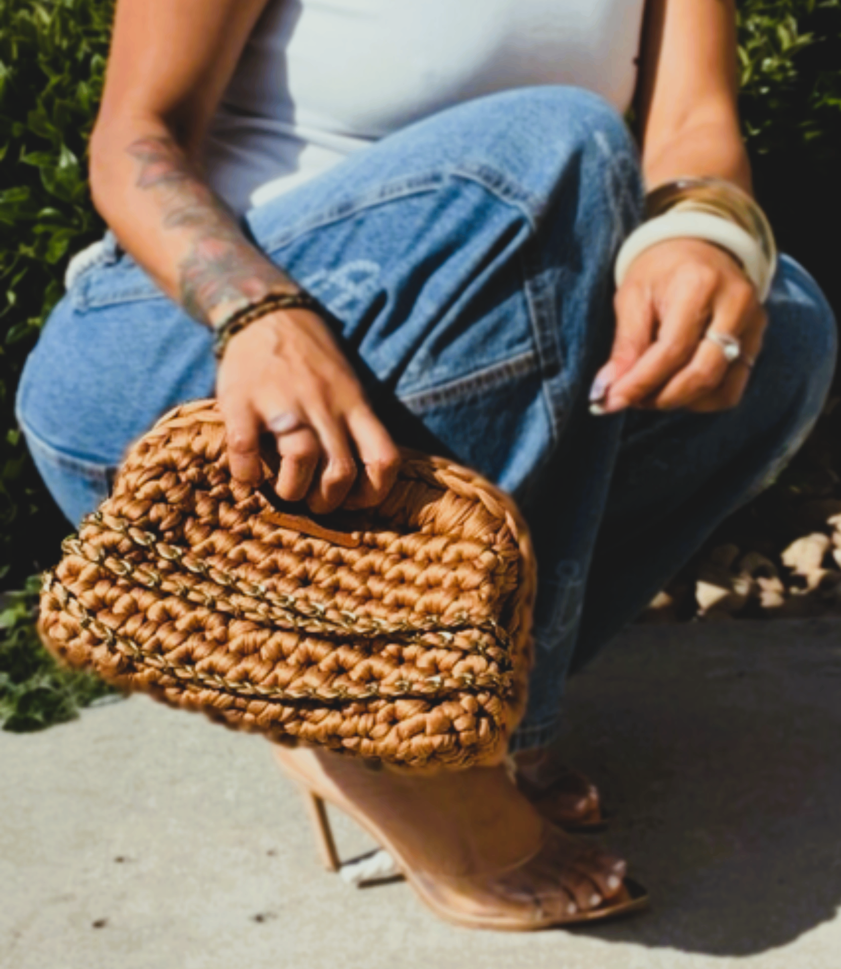 Tan crochet clutch with chain detail held while seated outdoors