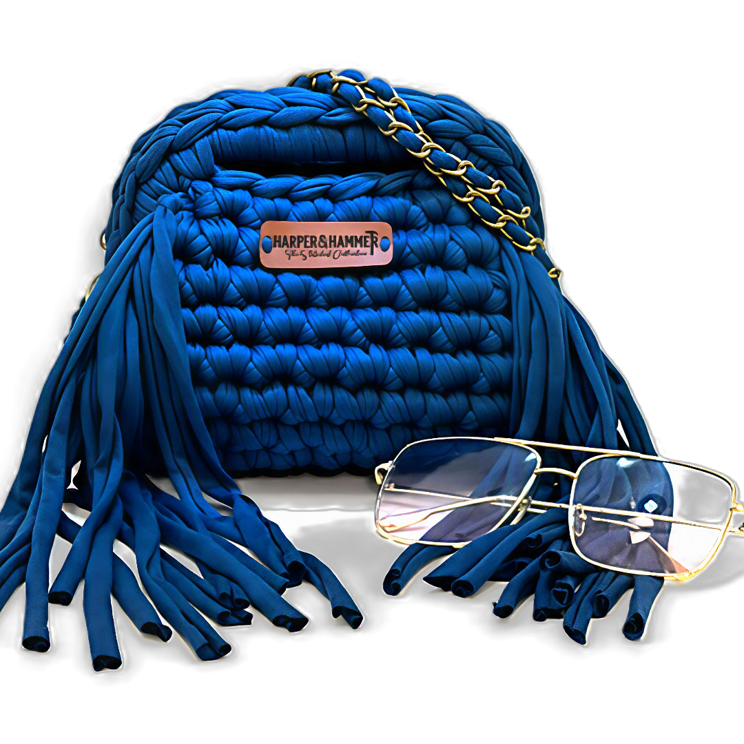 Blue crochet fringe bag with gold chain strap, Harper & Hammer leather tag, and gold-rimmed glasses